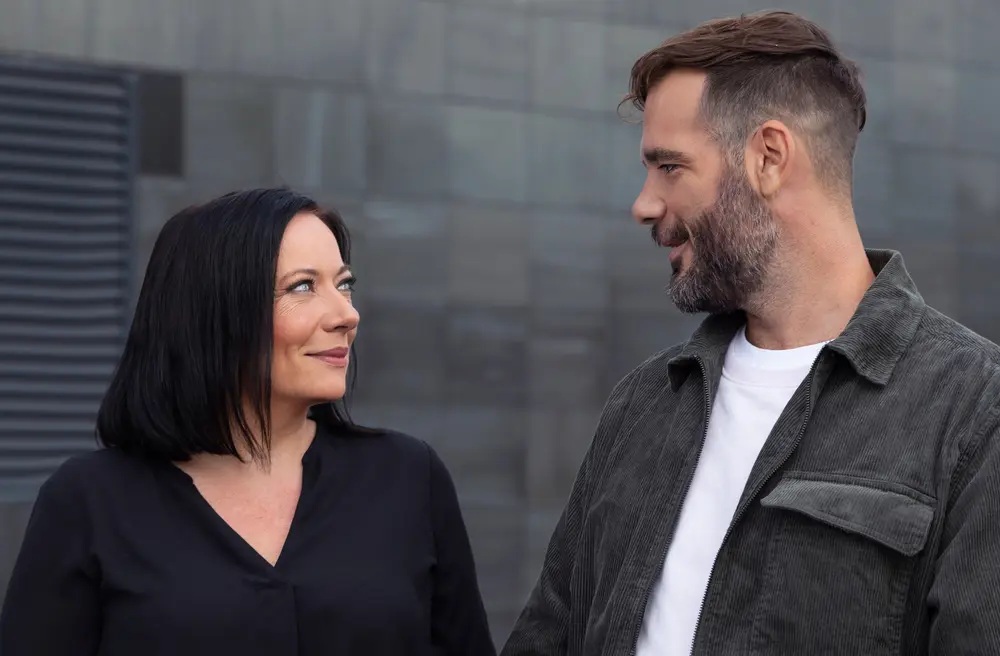 A man and a woman smiling at each other outside.