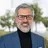 Hombre en traje azul y gafas sonriendo al aire libre