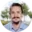 Retrato de un joven con vello facial y un moño, vistiendo una camisa azul, al aire libre