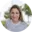 A woman with brown hair smiling, wearing a white polka dot shirt, against a blurred outdoor background.