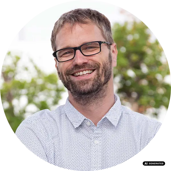 Ein bärtiger Mann mit Brille und einem gepunkteten Hemd lächelt im Freien.