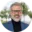 Confident grey-haired man in glasses wearing a blue blazer, smiling