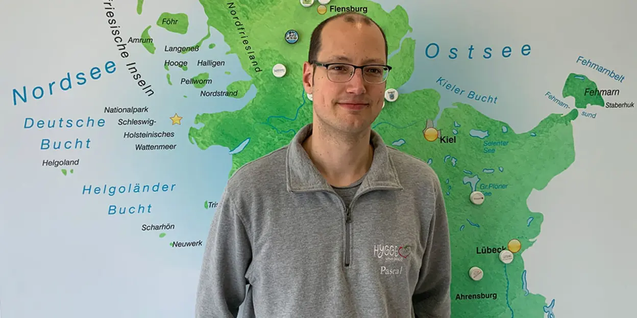 Persona con suéter gris con logo de Hygge frente a mapa de Schleswig-Holstein