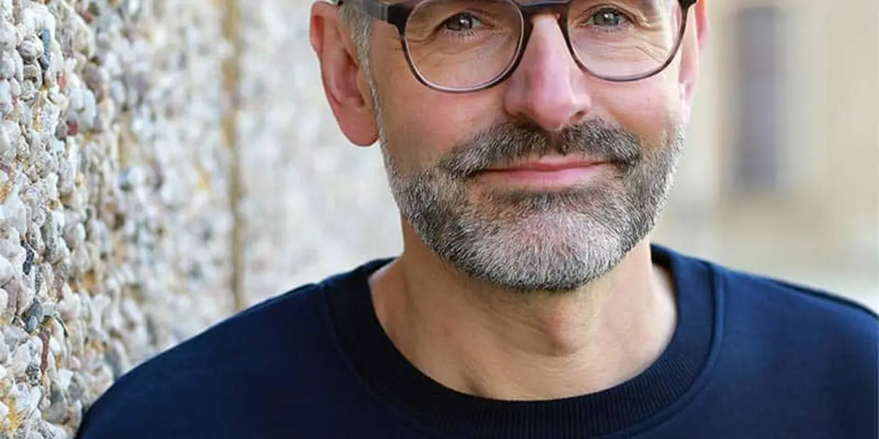 Lächelnder Mann mit Brille und dunklem Pullover draußen