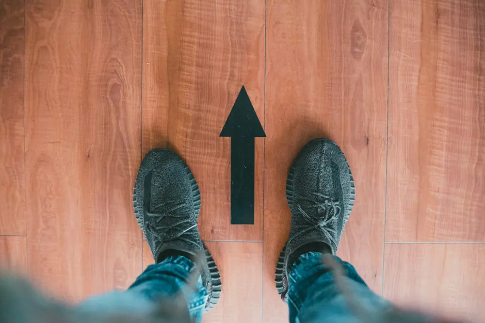 Füße in modischen Sneakers mit Pfeil auf Holzboden