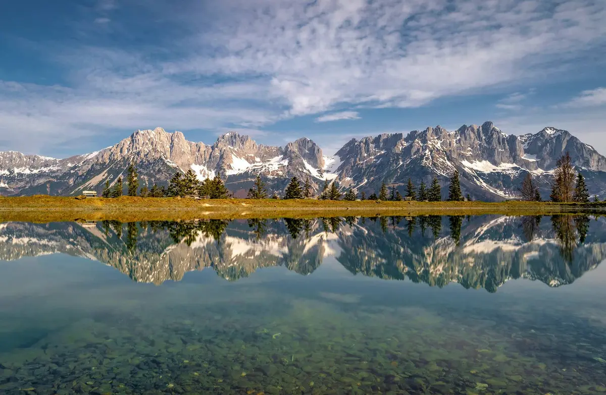 Beautiful mountains reflected in a clear, calm lake under a blue sky.