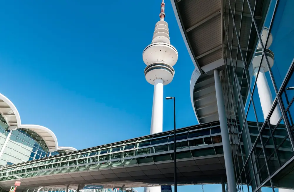 A tall tower against a clear blue sky, flanked by modern glass buildings.