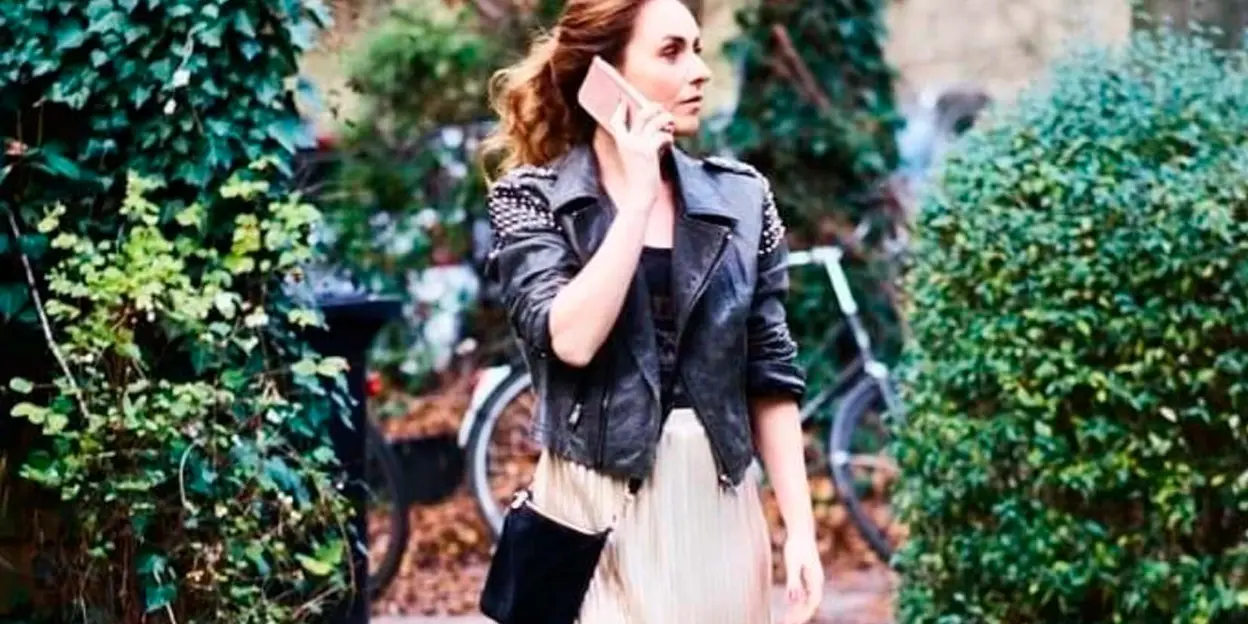 Woman in leather jacket and skirt talking on phone outdoors
