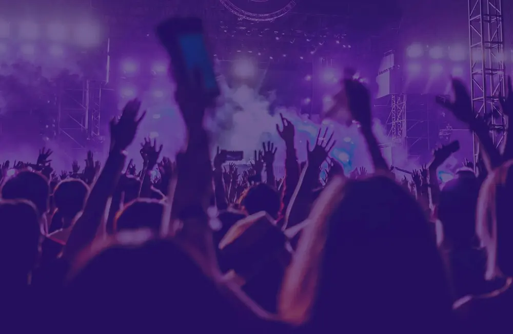 People raising hands at a lively concert with purple lights