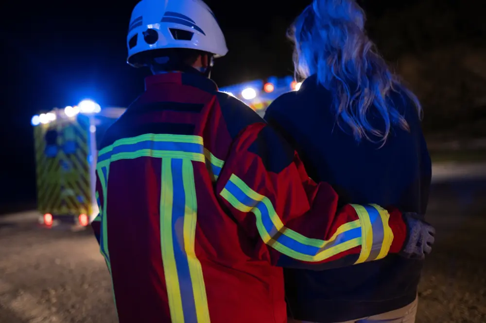 Responder in reflective gear assisting a person near an ambulance at night