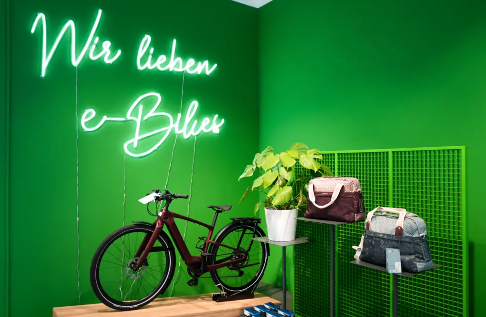 E-bike on stand with neon sign reading 'Wir lieben e-Bikes' and plant on green wall